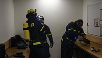 Drei Helfer/Helferinnen beim Anlegen der Atemschutzausrüstung