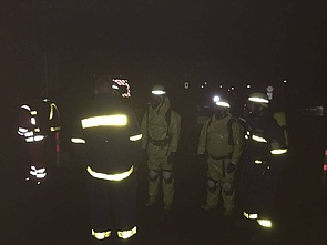 Mehrere Einsatzkräfte im Dunkeln. Die Personen sind fast ausschließlich aufgrund der reflektierenden Streifen auf der Einsatzkleidung zu erkennen.